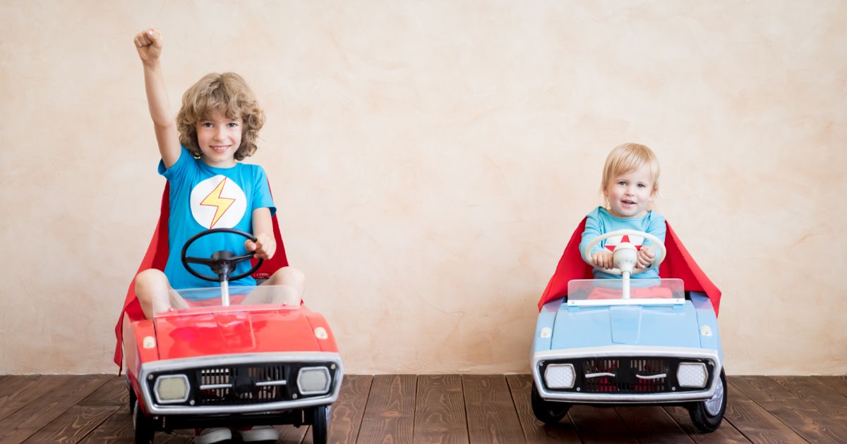 children in superhero costumes driving toy cars
